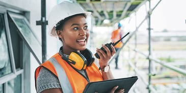woman in construction hat coordinating with team over radio